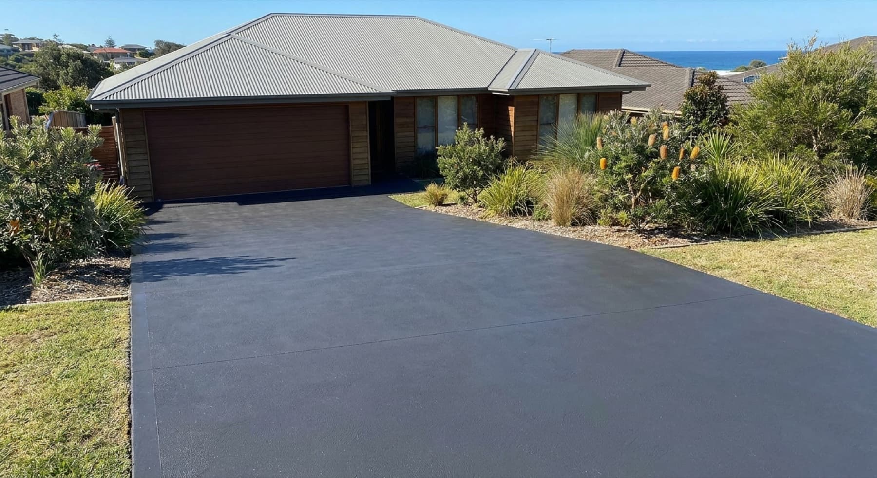 A colour-sealed coastal driveway holding a rich, even finish